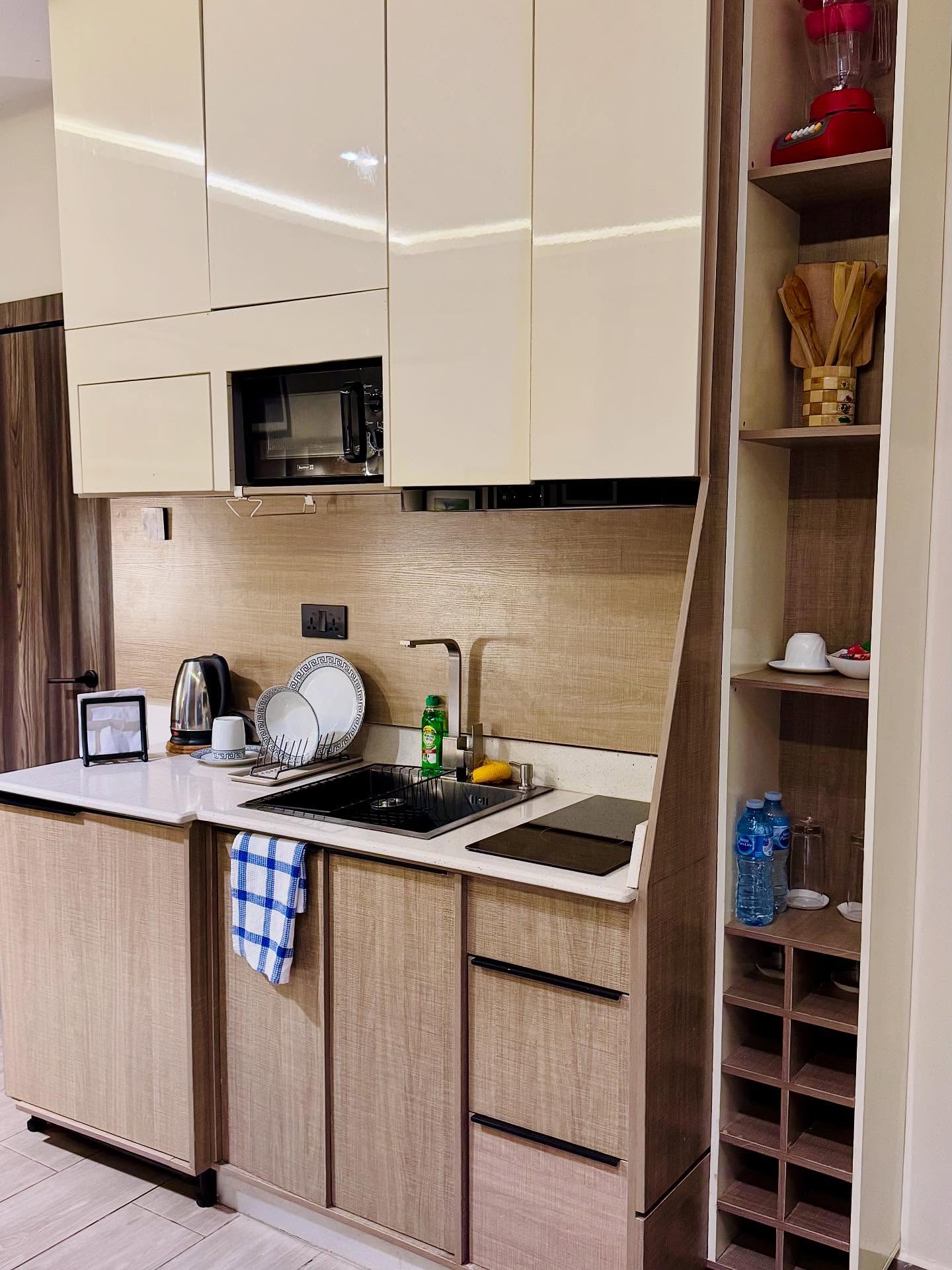 Kitchenette with a sink, cooktop, microwave, and storage inside a Seven Lugard apartment.